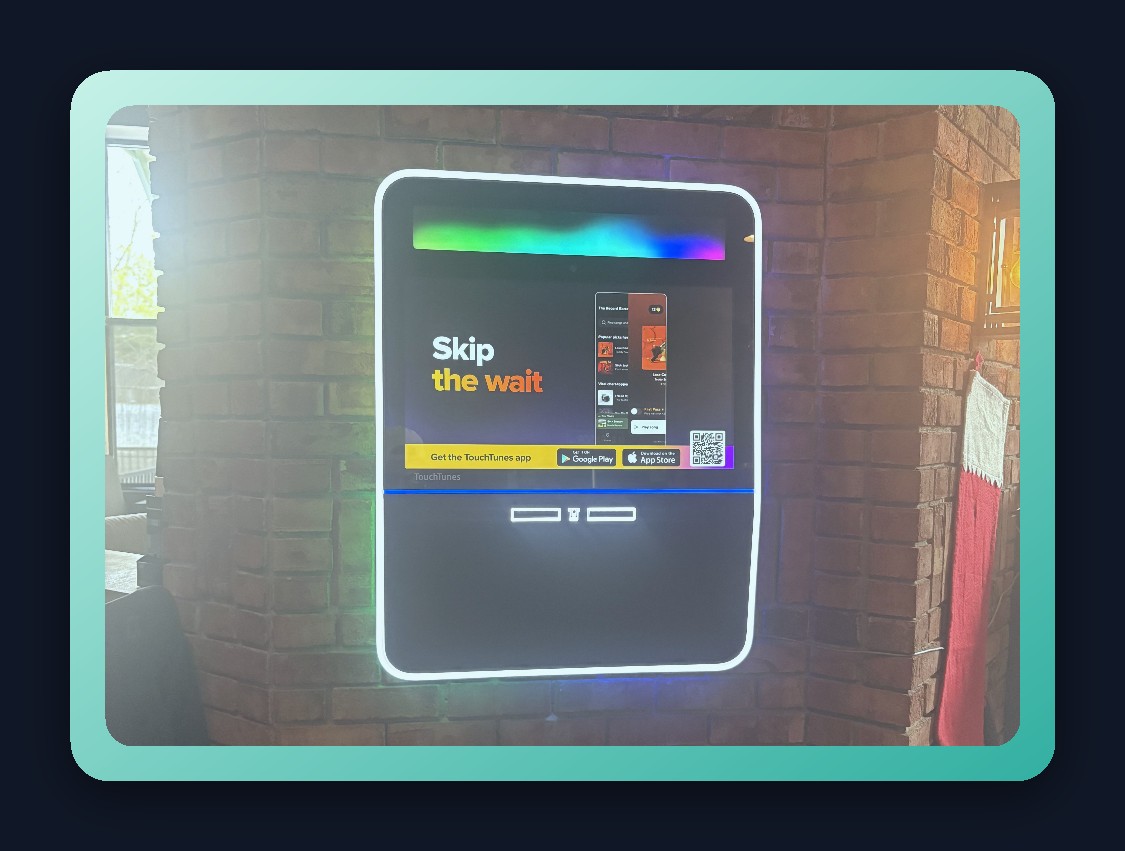 Wall-mounted digital jukebox installed on a brick wall in a bar