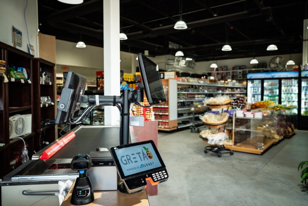 Grocery store checkout lane with GRETA POS touchscreen, scanner, and customer display